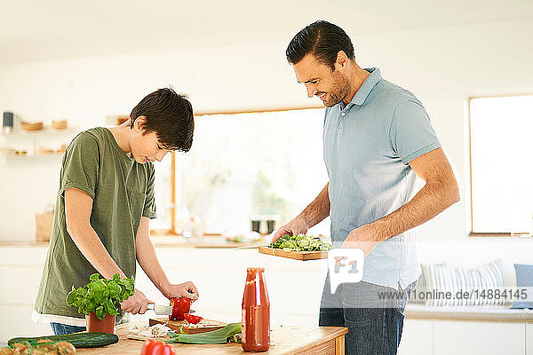 Junge schneidet rote Paprika an der Küchentheke  Vater schaut zu