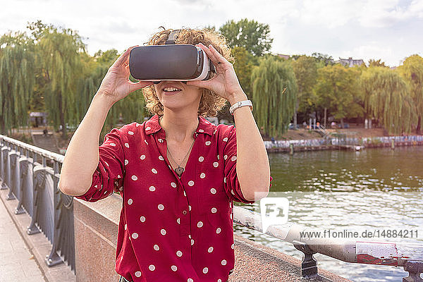 Junge Frau mit VR-Headset auf der Brücke Fluss im Hintergrund Berlin Deutschland