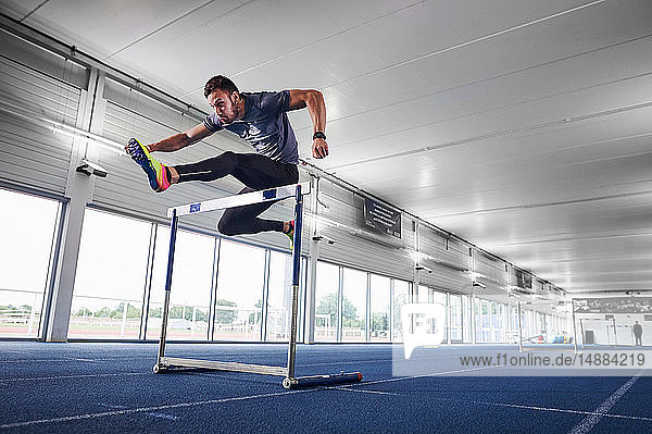 Athlet springt über Hürde auf Indoor-Laufbahn