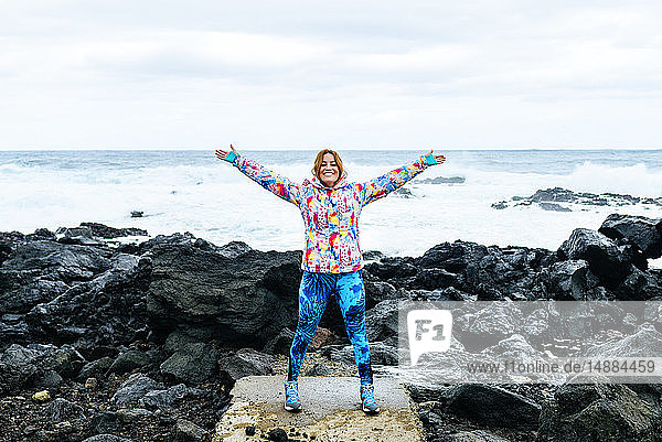 Portugal  Azoren-Inseln  Sao Miguel  Frau mit erhobenen Armen mit dem Meer im Hintergrund in felsiger Landschaft