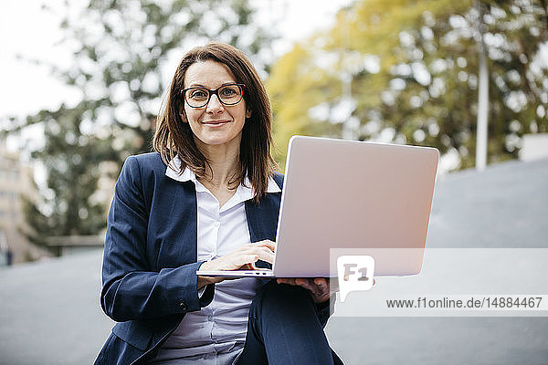Porträt einer lächelnden Geschäftsfrau in der Stadt mit Laptop