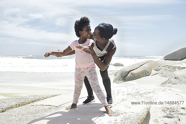 Mother and daughter doing a gymnastic exercise on the beach