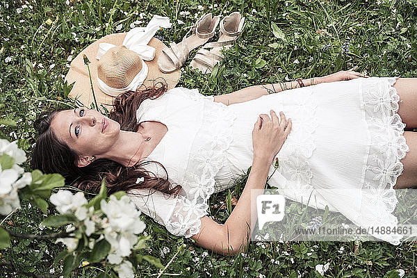 Porträt einer tagträumenden jungen Frau in weißem Spitzenkleid auf Blumenwiese liegend