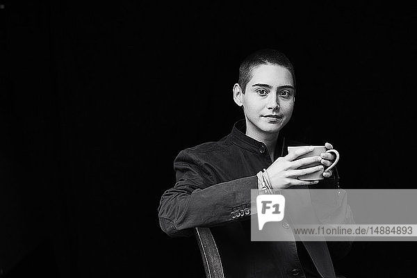 Portrait of sitting short-haired young woman holding cup of coffee