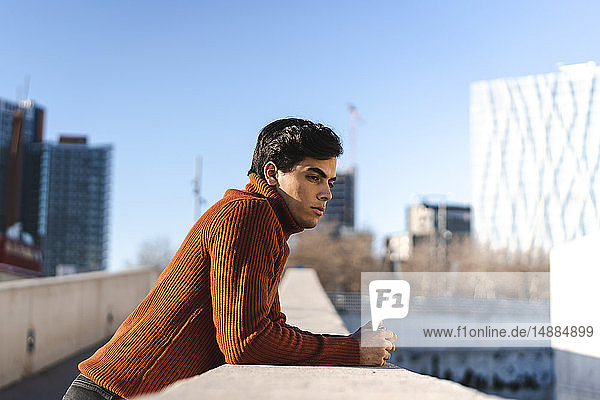 Modischer junger Mann mit Rollkragenpullover  der sich mit Abstand an eine Wand lehnt