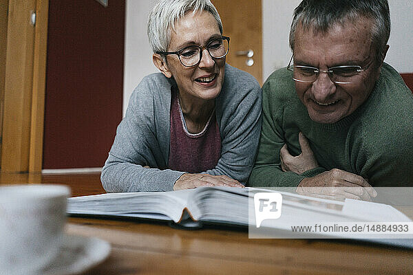 Älteres Ehepaar liegt zu Hause auf dem Boden und schaut sich ein Fotoalbum an