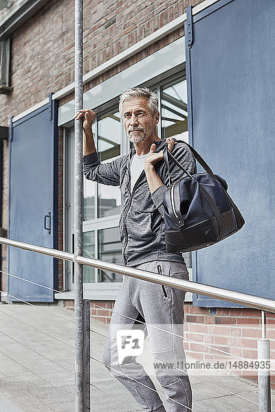 Porträt eines reifen Mannes mit Sporttasche vor der Turnhalle stehend