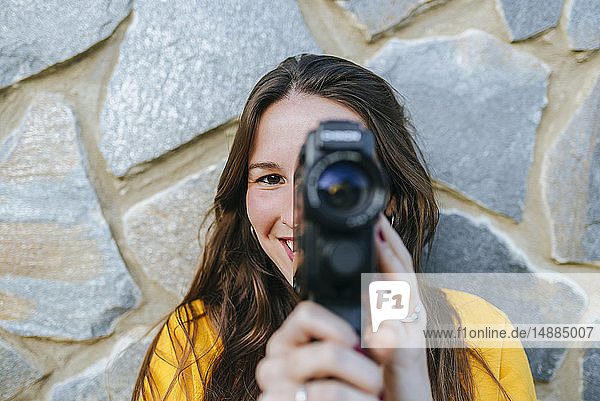 Porträt einer jungen Frau mit Oldtimer-Kamera an einer Steinmauer