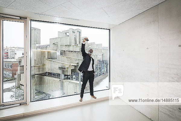 Barefoot businessman standing in front of window taking selfie with smartphone