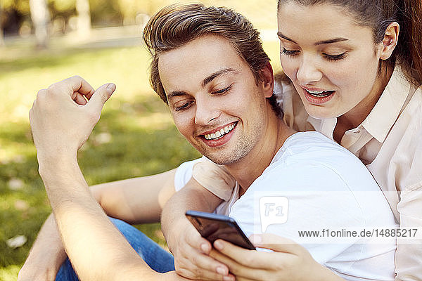 Junges Paar betrachtet Smartphone in einem Park