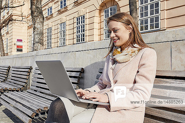 Österreich  Wien  lächelnde junge Frau sitzt mit Laptop auf Bank im MuseumsQuartier