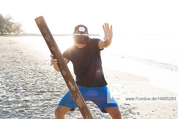 Man with wood pole wearing VR glasses on the beach