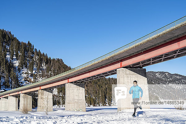 Deutschland  Bayern  sportlicher Mann läuft im Winter an einer Brücke