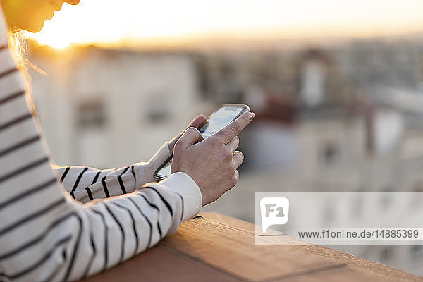 Junge Frau auf Balkon mit Mobiltelefon  Teilansicht