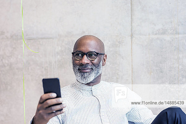 Porträt eines lächelnden reifen Geschäftsmannes mit Smartphone