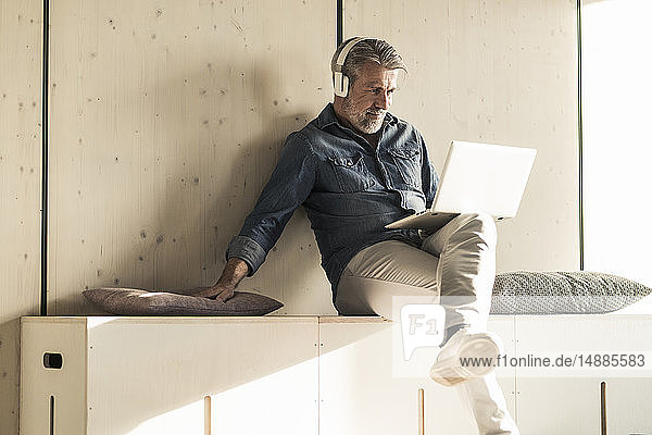 Lässiger reifer Geschäftsmann im Sitzen mit Laptop und Kopfhörern