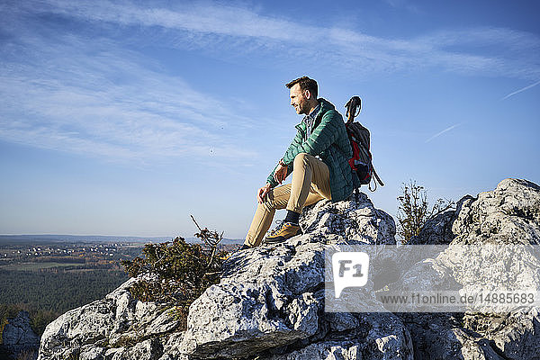 Mann auf Wanderung in den Bergen  der auf einem Felsen sitzt und die Aussicht genießt