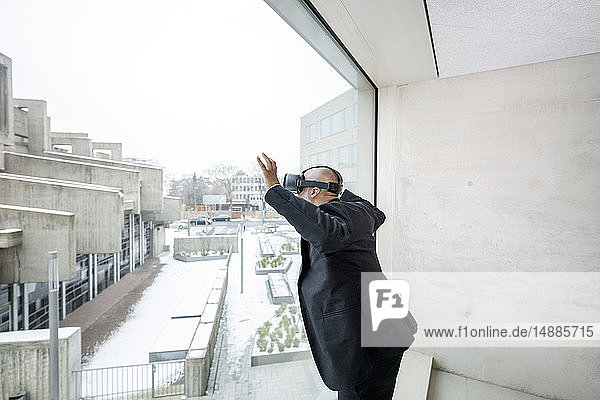 Reifer Geschäftsmann mit einer Virtual-Reality-Brille  die aus dem Fenster schaut