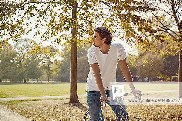 Junger Mann mit Fahrrad im Park  der sich umsieht