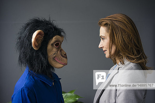 Geschäftsfrau steht einem Auszubildenden gegenüber  trägt eine Affenmaske und blauen Oevrall