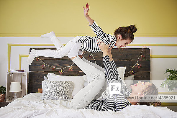 Mutter und Tochter spielen im Bett und tun so  als würden sie fliegen