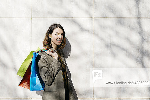 Porträt einer lächelnden Frau mit Einkaufstaschen an einer Wand stehend