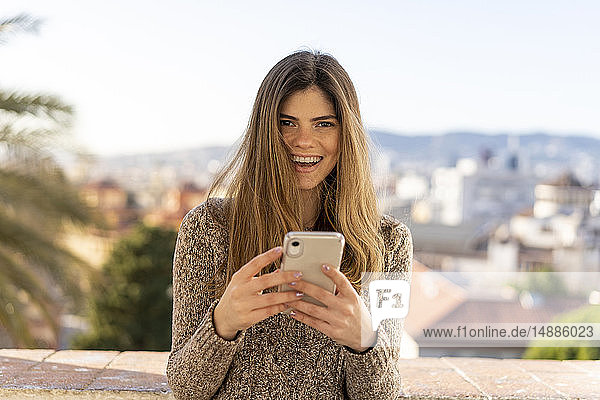 Porträt einer lachenden jungen Frau mit Handy in der Hand