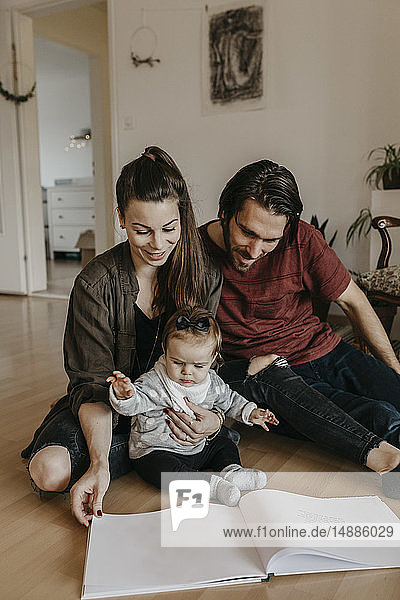 Glückliche Familie mit einem kleinen Mädchen  das zu Hause auf dem Boden sitzt und sich ein Fotoalbum ansieht