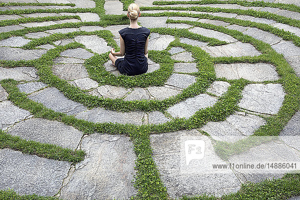 Italien, Südtirol, Lana, Frau sitzt in natürlichem Freiluftlabyrinth und meditiert