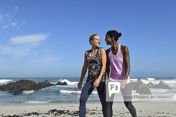 Zwei glückliche Frauen gehen am Strand spazieren