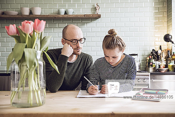 Father and daughter sitting in kitchen  doing homework