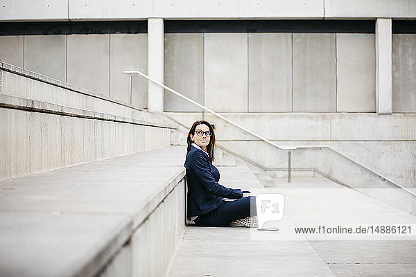 Geschäftsfrau sitzt im Freien auf einer Treppe mit Laptop