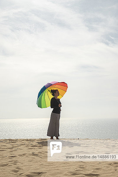 Frau mit buntem Regenschirm am Strand stehend