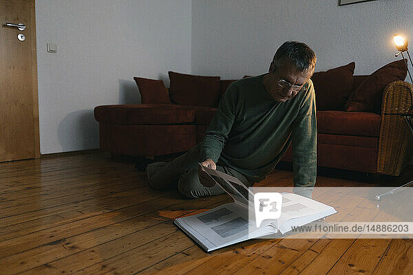 Älterer Mann sitzt zu Hause auf dem Boden und schaut sich ein Fotoalbum an
