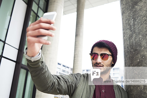 Porträt eines stilvollen Mannes mit Sonnenbrille und violettem Hut  der sich per Mobiltelefon selbstständig macht