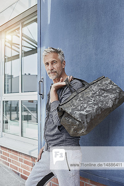 Portrait of mature man with camouflage sports bag standing in front of gym