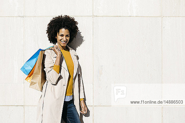 Porträt einer lächelnden Frau mit Einkaufstaschen an einer Wand stehend