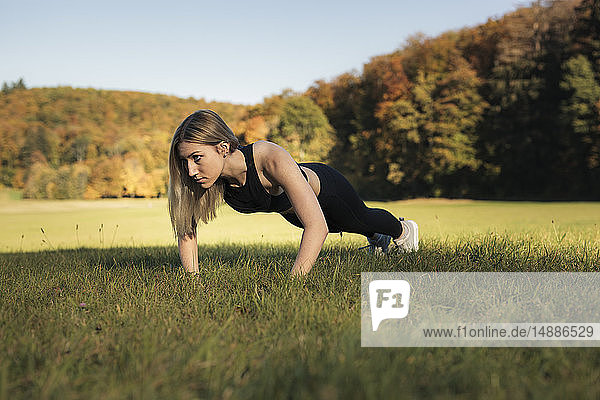 Young woman doing pushups during workout on meadow