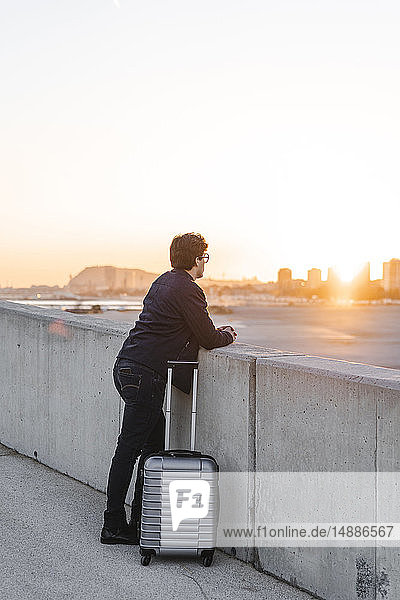 Spanien  Barcelona  junger Geschäftsmann mit rollendem Koffer beim Sonnenuntergang