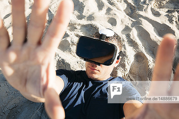 Man wearing VR glasses lying in sand on the beach
