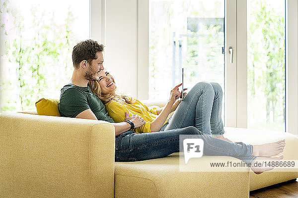 Paar  das in seinem neuen Zuhause auf der Couch sitzt und ein digitales Tablet benutzt
