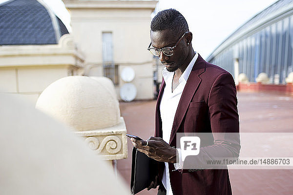 Junger Unternehmer  der auf der Hotelterrasse seinen Termin mit einem Smartphone wahrnimmt