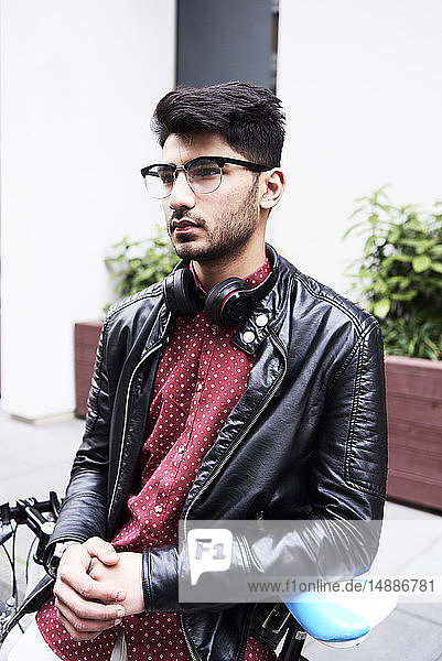 Portrait of handsome man in leather jacket and glasses with headphones  leaning on fixie