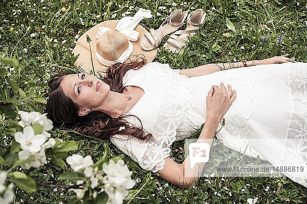 Porträt einer tagträumenden jungen Frau in weißem Spitzenkleid auf Blumenwiese liegend