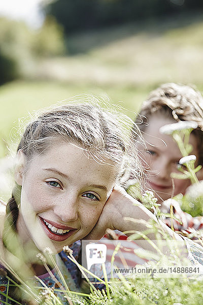 Portrait of smiling girl lying on a meadow with little brother at the background