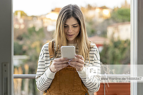 Porträt einer jungen Frau  die auf dem Balkon steht und auf ein Handy schaut
