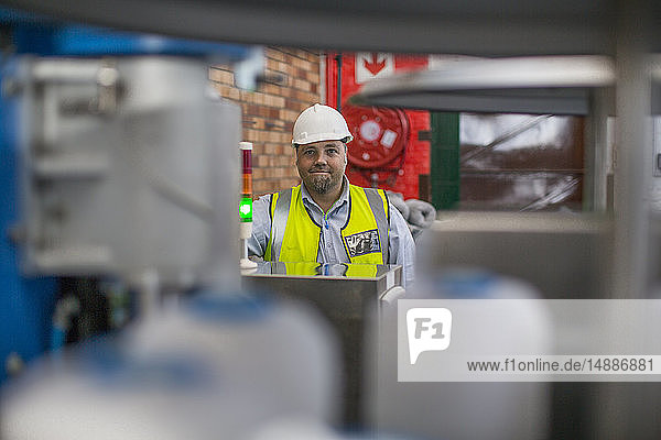 Porträt eines lächelnden Mannes mit reflektierender Weste und Schutzhelm in einer Fabrik
