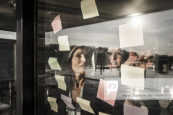 Zwei Geschäftsfrauen machen ein Brainstorming und kleben Haftnotizen an die Fensterscheibe
