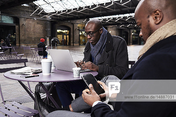 Zwei Geschäftsleute sitzen am Tisch eines Cafés und benutzen mobile Geräte