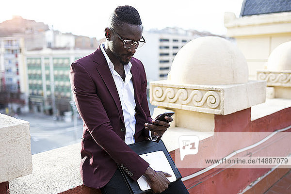 Junger Unternehmer  der auf der Hotelterrasse seinen Termin mit einem Smartphone wahrnimmt